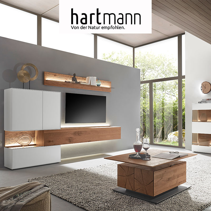 Hartmann TORIDO - Wohnzimmermöbel aus massiver Birke weiß lackiert kombiniert mit Kerneiche Umato. Ambientebild zeigt Holz-Lowboard eingefasst in weißes Standelement darüber Holz-Wandpaneel, im Vordergrund passender Holzcouchtisch.