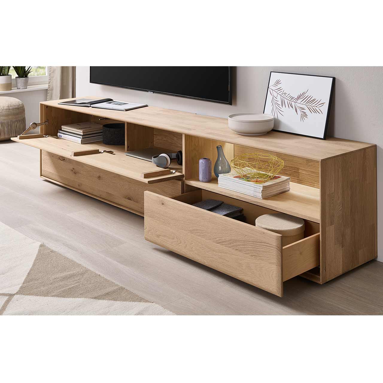 Modernes Lowboard aus massiver Kerneiche Natur mit einem offenem Schubkästen rechts unten, einer darüber beleuchteten Nische mit geschroppter Rückwand und einer offenen Klappe links.