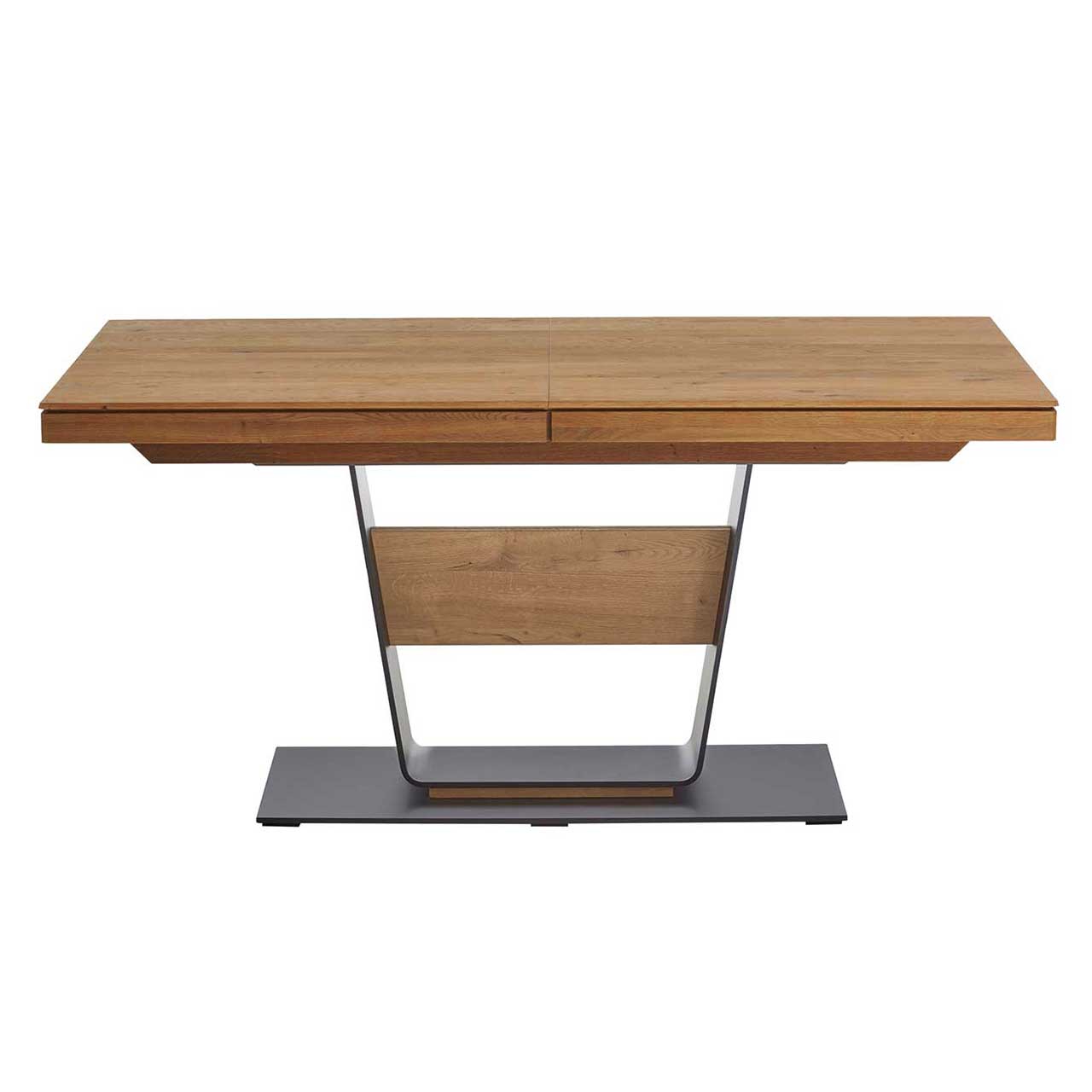 Moderner Esstisch mit rechteckiger Tischplatte aus massiver Kerneiche Umato. Das Gestell besteht aus einer V-förmigen Stahlsäule mit mittigem Holzelement und steht auf einer dunkelgrauen Metallbodenplatte.