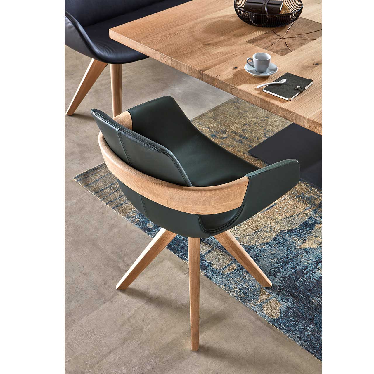 Detailaufnahme der Rückseite eines Esszimmerstuhls mit Holz-Applikation im Lendenbereich, bezogen mit dunkelgrünem Leder auf Holzgestell.