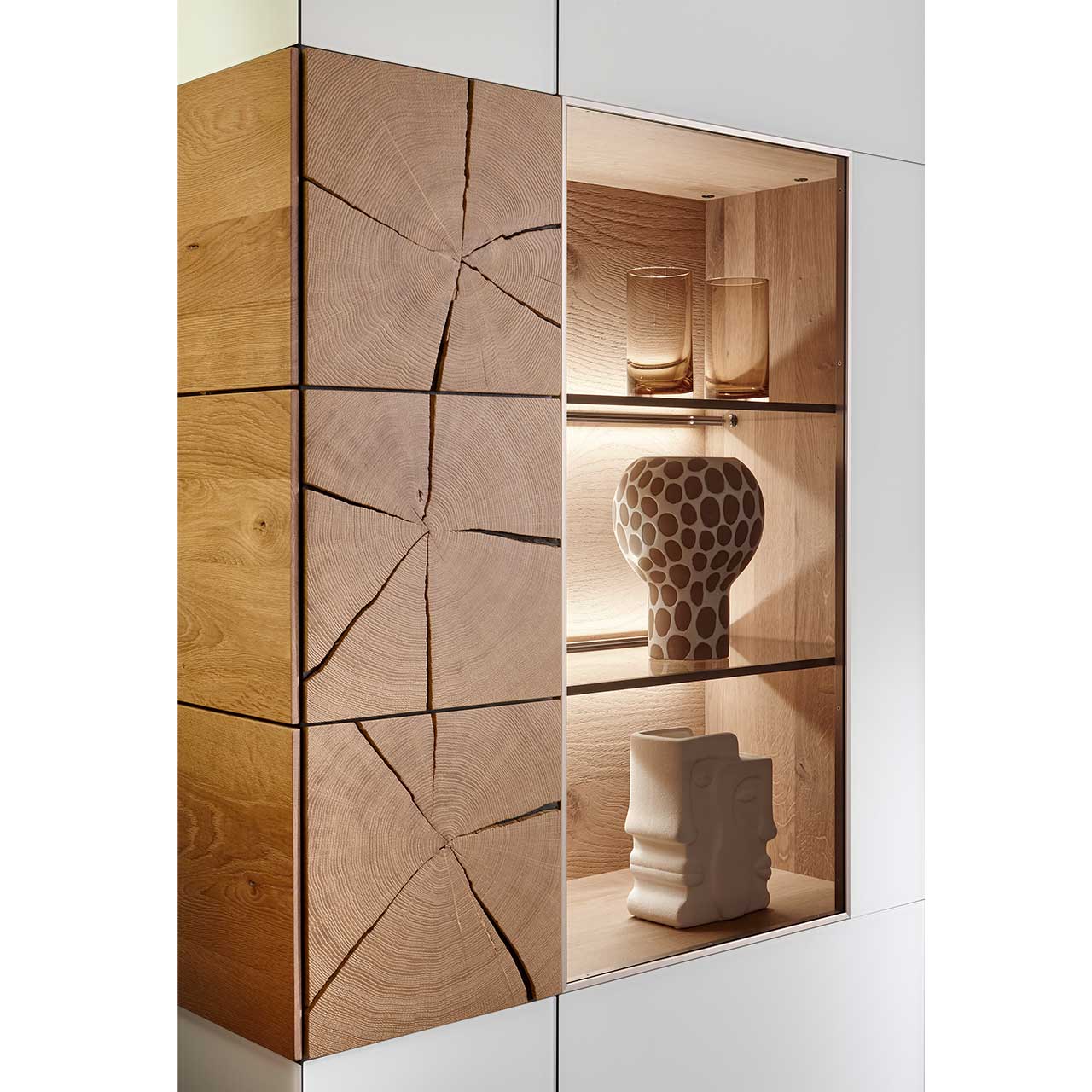 Detailaufnahme des CAYA Highboards Nr. 7170-7084W mit links einer Holztür mit drei vertikal verlaufenden Hirnholzscheiben und rechts einer Glastür mit drei beleuchteten Böden.