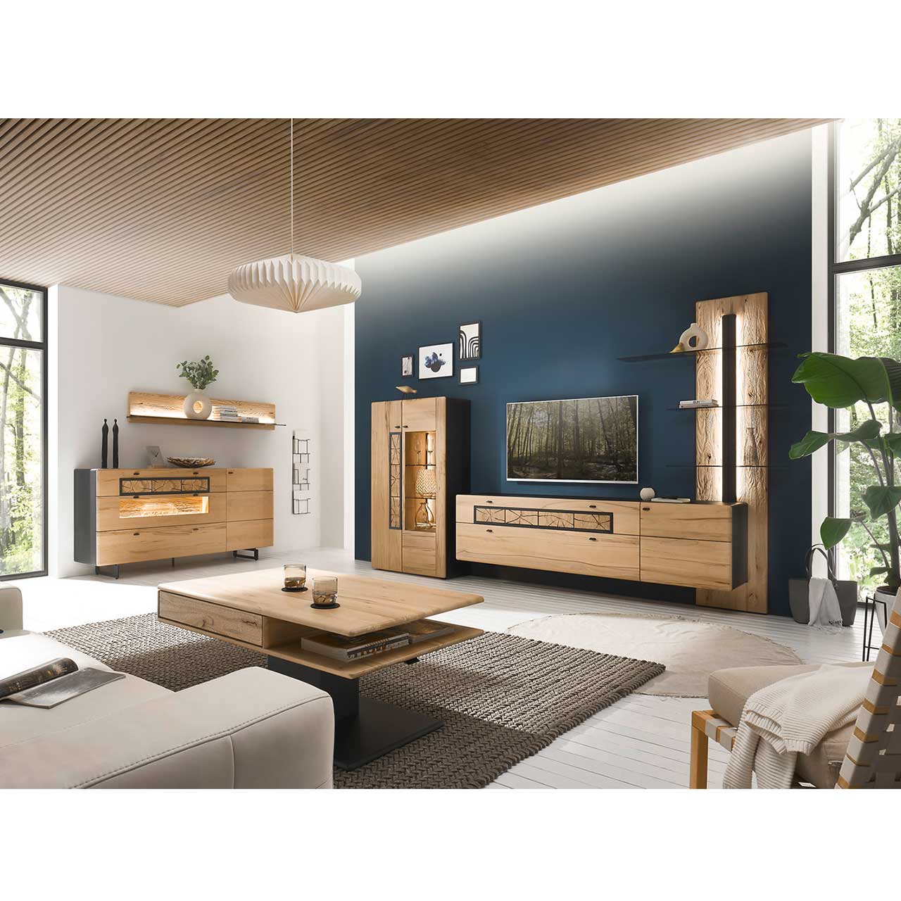 Eingerichtetes Wohnzimmer mit moderner Wohnwand aus Kernbuche vor einer dunkelblauen Wand bestehend aus Highboard, Lowboard und Paneel. Links das passende Sideboard auf Metallkufen darüber ein Regal. Im Vordergrund der dazugehörige Couchtisch.