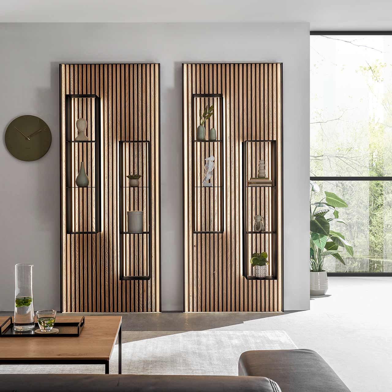 Zwei moderne Wandpaneele mit Lamellenrückwand aus hellem Holz. Darauf befestigt je zwei Metallregale mit Ablageböden in anthrazit. Im Vordergrund links der passende Couchtisch mit filigranem Metallgestell.