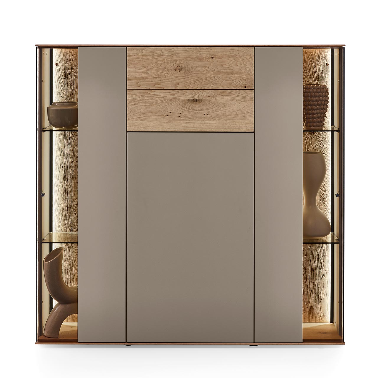 Hartmann Möbel SVEA - Highboard 8660-7141 - Kerneiche Natur, Lack San Modernes Highboard aus massiver Kerneiche Natur mit Lackfronten in Sand und Riffholz. Mit einer Lacktür, einem Schubkasten mit Riffholzfront und zwei Glas-Lacktüren mit edler, beleuchteter Riffholzrückwand - in Frontansicht.