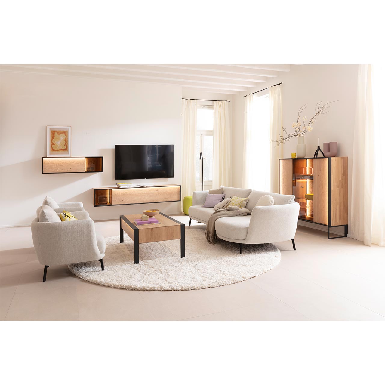 Eingerichtetes Wohnzimmer mit Massivholzmöbeln aus heller Kerneiche Natur: Highboard auf Metallkufen anthrazit mit beleuchteter Front und Glastüren, schlichtes Hängelowboard, Hängeschrank mit Glasausschnitt und passender Holz-Couchtisch auf Metallfüßen. 