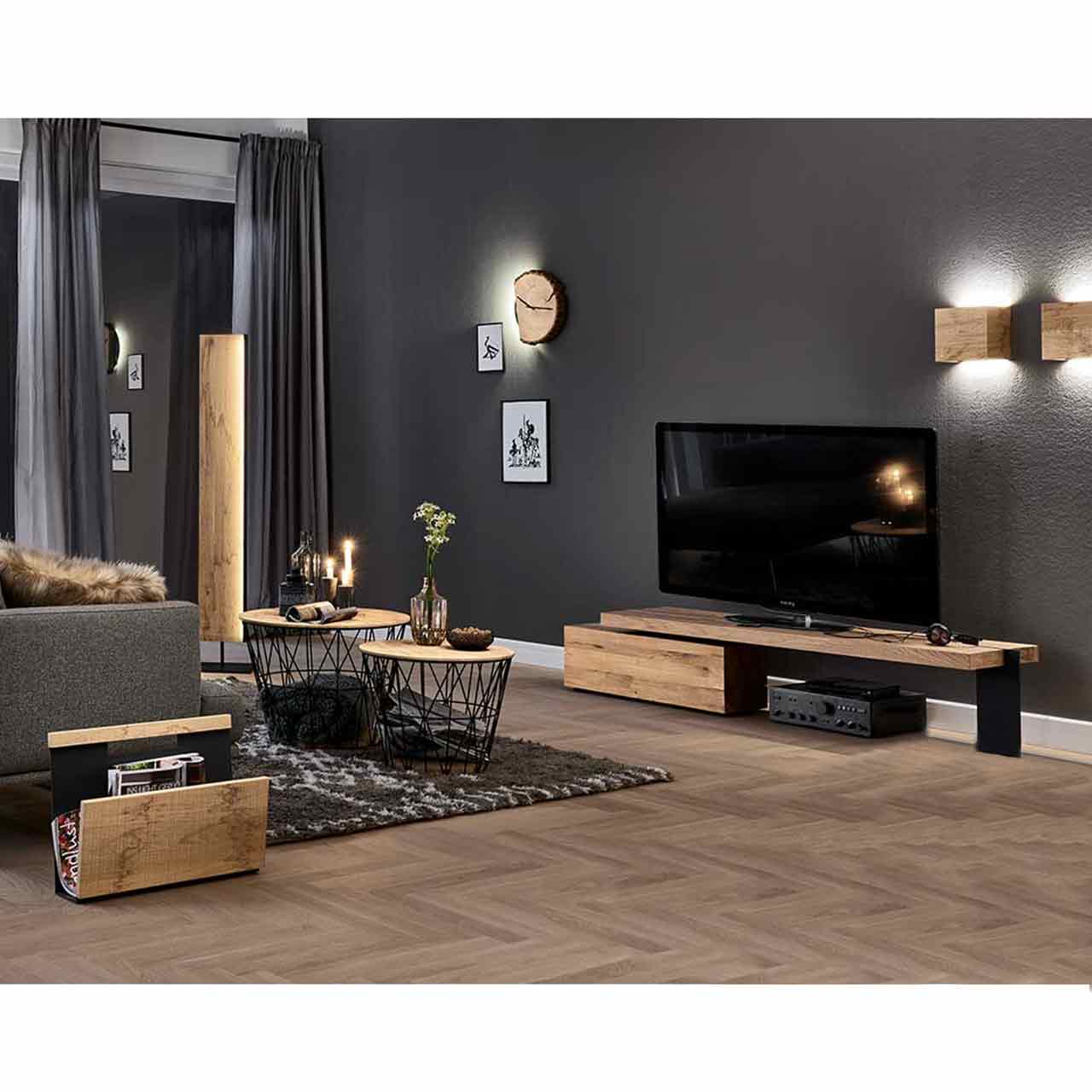 Wohnzimmer mit Lowboard und Fernseher. Darüber zwei Holzwandampen und Holzuhr - an grauer Wand. Links daneben eine Holzstehlampe, davor zwei runde Couchtische mit Korb-Metallgestell und Holz-Zeitungsständer.
