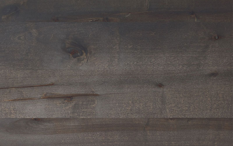 Hartmann Möbel - Holz-Kachel Kernbirke anthrazit gebeizt Holz-Kachel in Kernbirke anthrazit gebeizt mit lebendiger Maserung – sichtbare Holzstruktur mit feinen Rissen, Oberfläche in dunklem Graubraunton.