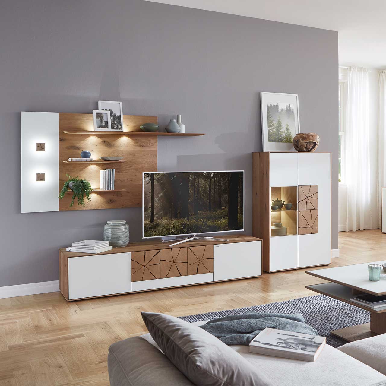 Wohnzimmer mit moderner dreiteiliger Massivholz Wohnwand mit Mattglas weißen Fronten und dekorativen Hirnholzscheiben: Langes Lowboard mit Hirnholz und Kufen, Wandpaneel mit Regalböden, Highboard mit beleuchtetem Glasausschnitt und Hirnholz.
