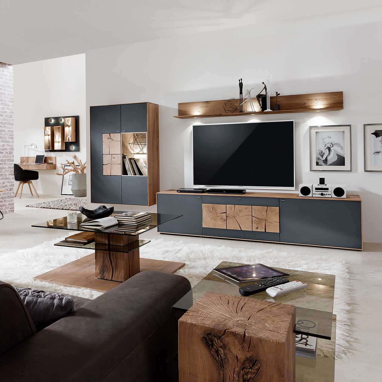 Hartmann CAYA - Hängeelement 7170-7091A li. Wohnzimmer mit moderner dreiteiliger Massivholz Wohnwand mit Mattglas Anthrazit Fronten und dekorativen Hirnholzscheiben: Lowboard mit Hirnholz, Wandregal mit Spotbeleuchtung, große Hängevitrine mit beleuchtetem Glasausschnitt und Hirnholz.