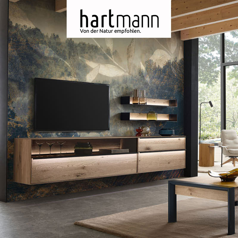 Hartmann ANEA - Massivholzmöbel aus Kerneiche Natur sandgestrahlt kombiniert mit Metall anthrazit. Ambientebild zeigt zwei schlichte Hängelowboards mit Glasblende, darüber hängend zwei Metallregale mit edler Riffholzrückwand - vor dezenter Motivtapete