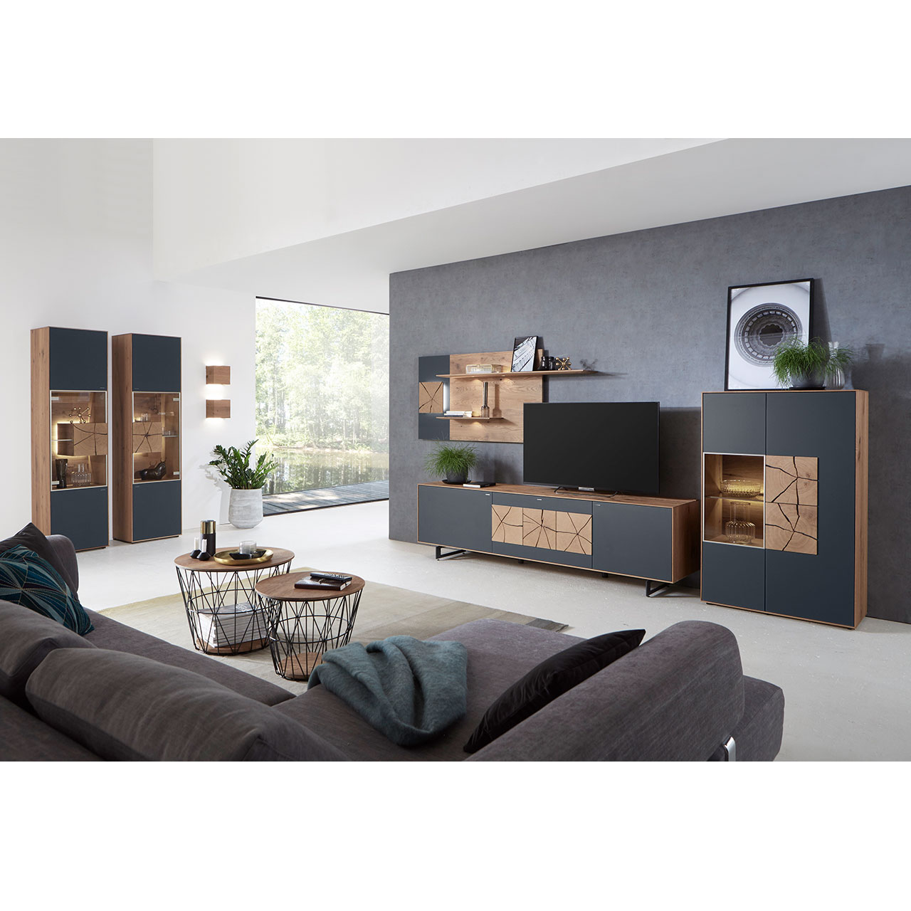 Wohnzimmer mit moderner Massivholz Wohnwand mit Mattglas Anthrazit Fronten und dekorativen Hirnholzscheiben: Lowboard auf Kufen, Wandpaneel mit Regalböden und beleuchtete Standvitrine, links zwei passende Hochvitrinen, davor zwei runde Couchtische.