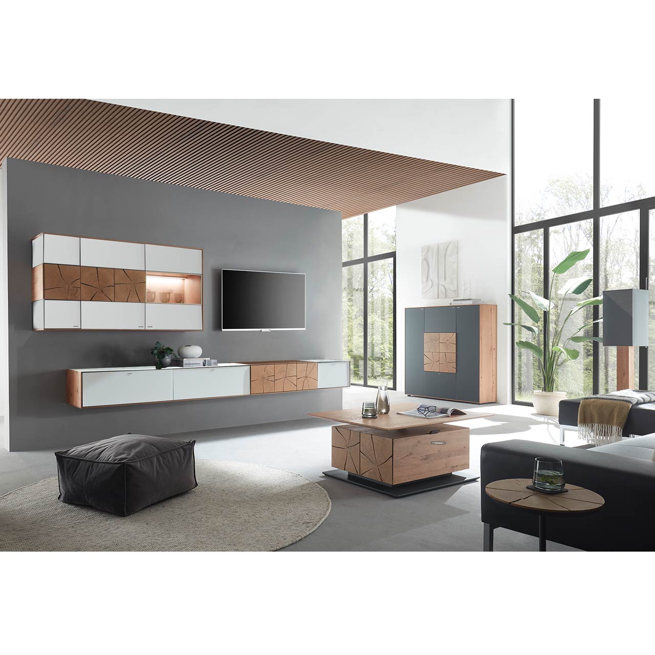 Wohnzimmer mit TV und moderner Wohnwand aus massiver Kerneiche und Mattglas weiß Fronten, mit schmalem Hängelowboard und beleuchteter Hängevitrine. Rechts das passende Highboard. Im Vordergrund ein rechteckiger Holz-Couchtisch.