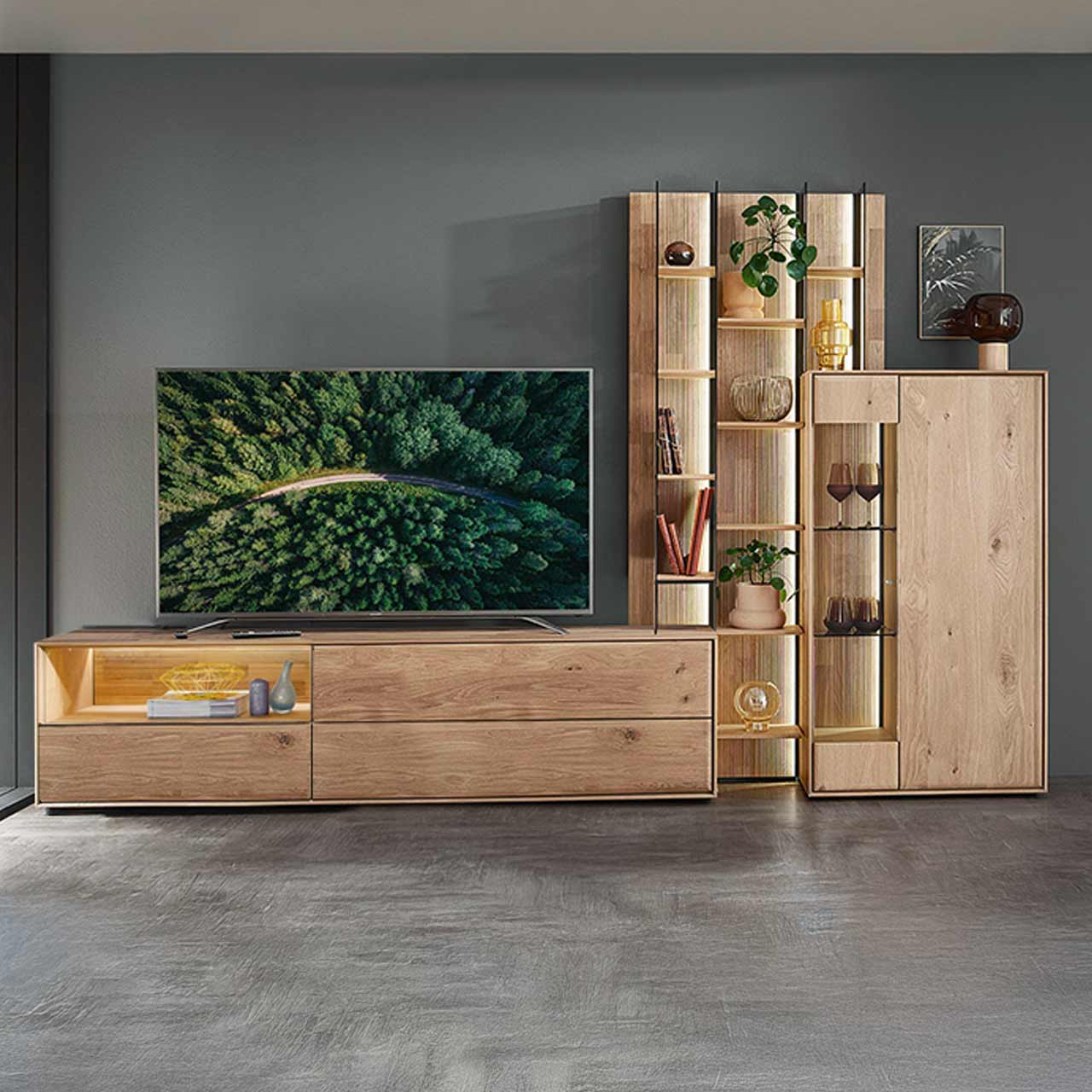 Moderne dreiteilige Wohnwand aus massiver Kerneiche Natur bestehend aus einem Highboard mit Glastür, einem hohen Wandregal mit Holzböden, beleuchteten Glasseiten und geschroppter Rückwand und einem darin integriertem Lowboard mit Nische.