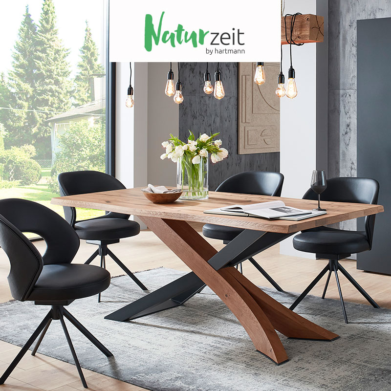 Hartmann NATURZEIT - moderne Esszimmermöbel aus massivem Holz kombiniert mit Glas und Metall. Ambientebild zeigt rechteckigen Esstisch mit Kreuzgestell umgeben von vier komfortablen Stühlen in schwarzem Leder mit Vier-Fuß Metallgestell in anthrazit.