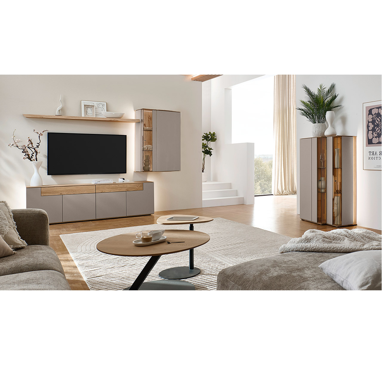 Hartmann Möbel SVEA - Wohnkombination 8660 Nr. V24 SV - dreiteilig aus Kerneiche Natur, Lack Sand - Milieubild Wohnzimmer mit moderner Massivholzwohnwand bestehend aus einem Lowboard mit Schubkästen, einer Hängevitrine sowie einem Wandboard - im asymmetrischen Design. Rechts passendes Highboard mit Glastüren, davor Holz-Couchtisch.
