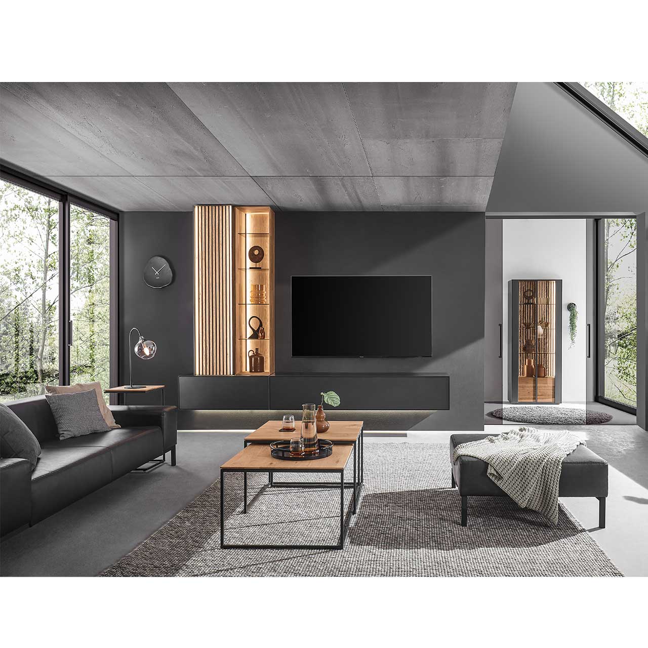 Modern eingerichtetes Wohnzimmer mit vierteiliger Wohnwand in Anthrazit kombiniert mit hellem Holz und Lamellen. Mit passendem Sideboard rechts. Im Vordergrund zwei ineinander geschobene minimalistisch Couchtische mit Holzplatte und Metallgestell.
