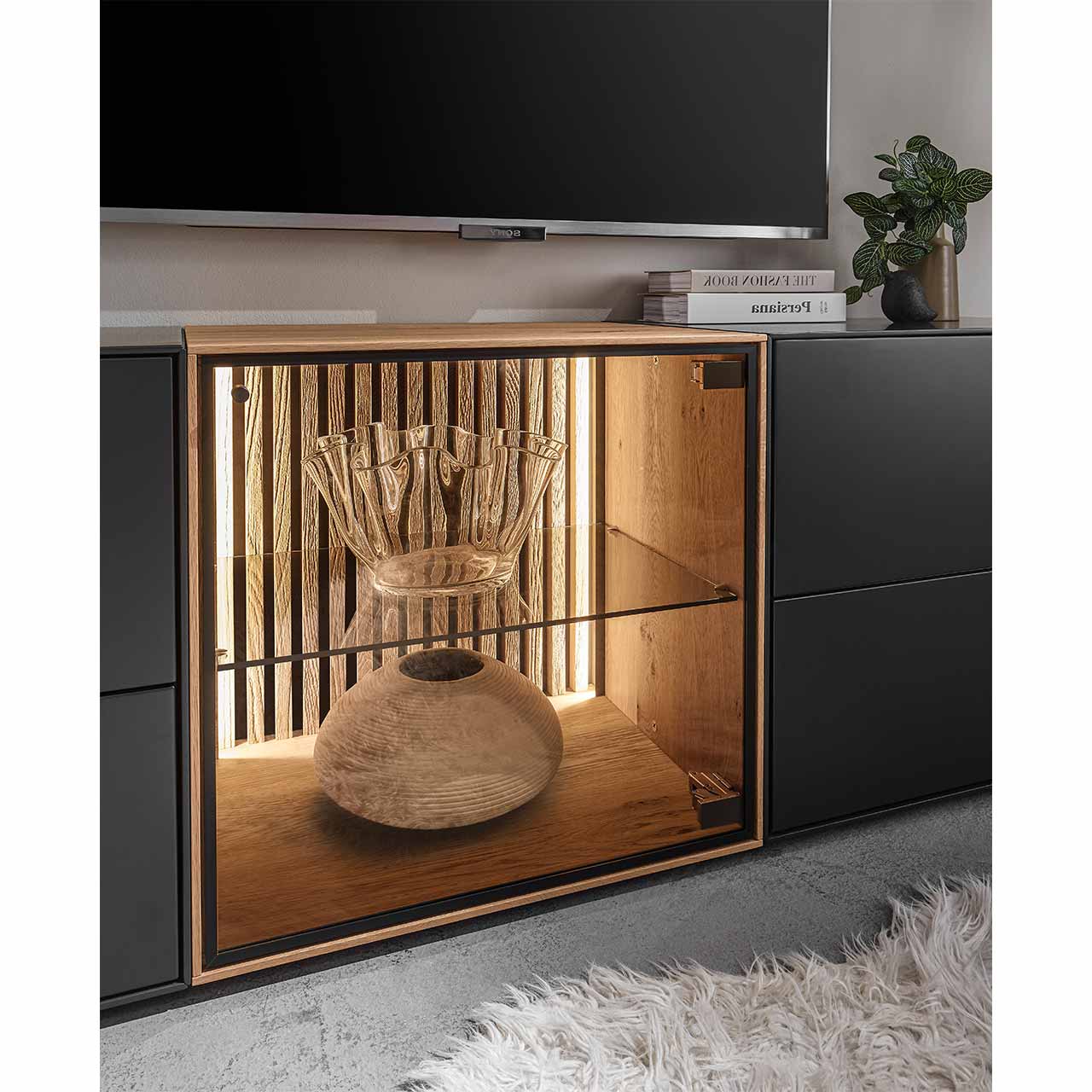 Detailaufnahme einer quadratischen Lowboard-Vitrine aus hellem Holz mit beleuchteter Lamellenrückwand und Glaseinlegeboden - Bildausschnitt aus Wohnwand.