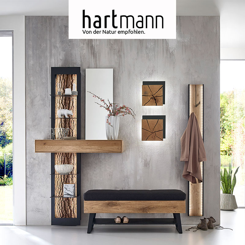Hartmann GARDEROBEN - Möbel aus massivem Holz wahlweise mit weißen Fronten kombiniert mit Metall anthrazit und dekorativen Holzelementen. Ambientebild zeigt Standregal mit Spiegel und Schubkasten, Polstersitzbank, zwei Wandlampen und Garderobenpaneel.