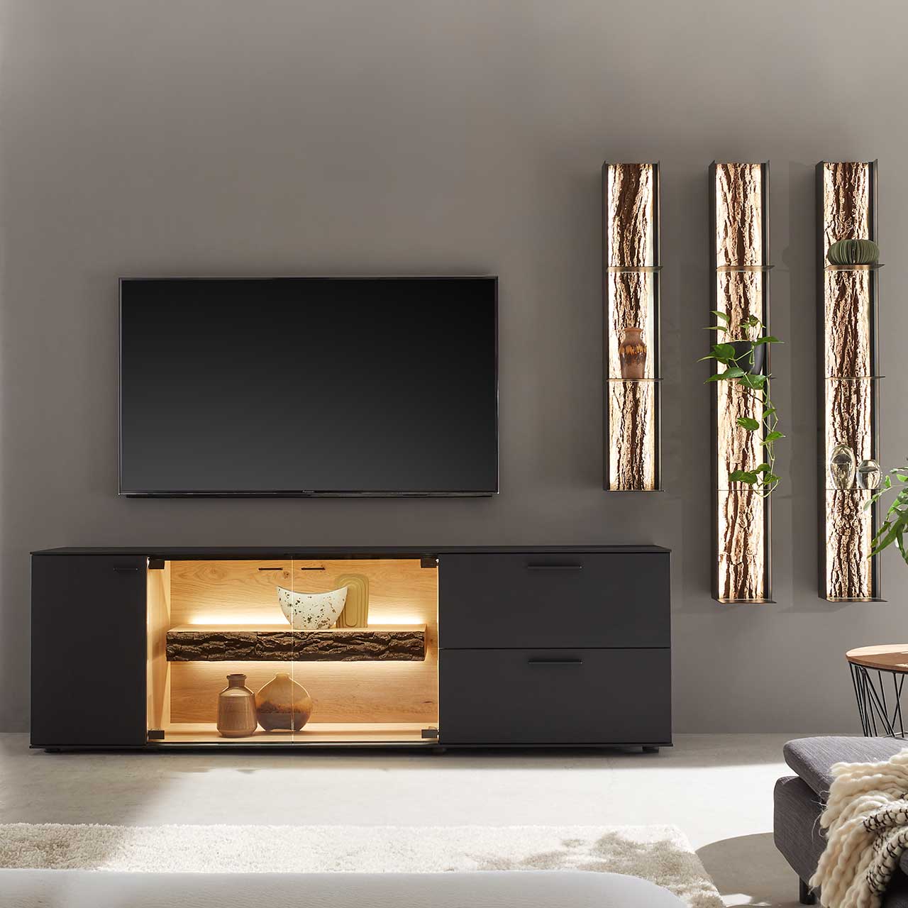 Moderne vierteilige Wohnwand bestehend aus einem Lowboard aus massiver Kerneiche Natur, anthrazit gebeizt mit beleuchtetem Glasausschnitt und drei modernen Wandregale aus Metall mit sichtbarer Baumrinde.