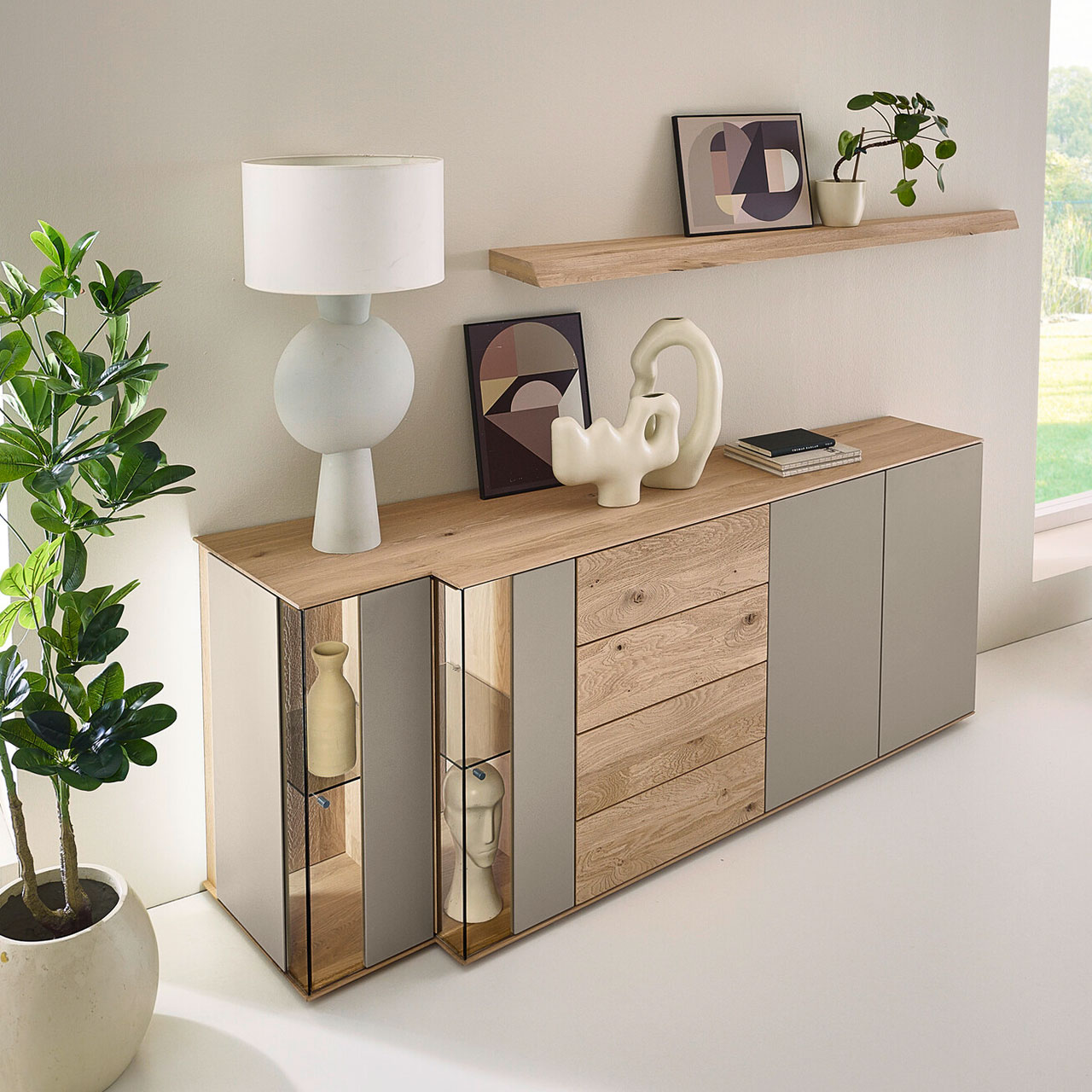 Moderne Kommode aus massiver Kerneiche mit Lackfronten Sand und Riffholz. Mit Lacktüren, Schubkasten und Tür mit Riffholzfront sowie zwei Glas-Lacktüren in asymmetrischem Design und beleuchteter Riffholzrückwand. Darüber Riffholz-Wandboard.