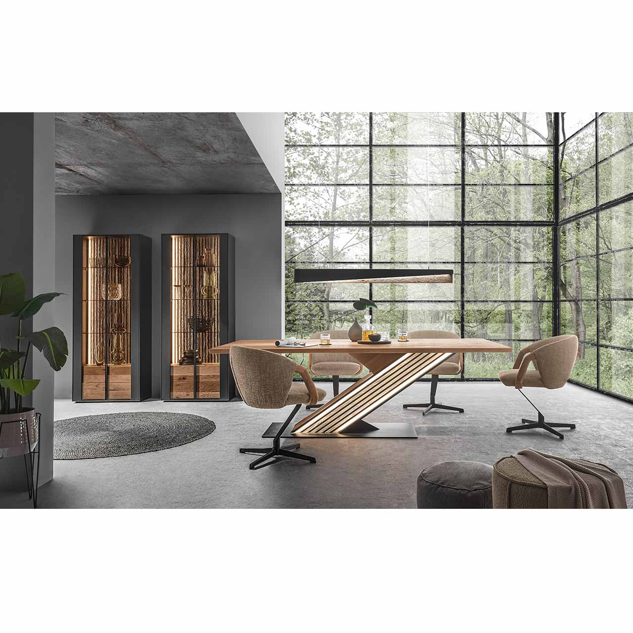 Modern eingerichtetes Esszimmer mit Esstisch aus hellem Holz mit beleuchteter Mittelsäule mit Massivholz-Lamellen auf anthrazitfarbener Bodenplatte. Umgeben von drei modernen Stühlen in hellem Stoff und Metallgestell. Links daneben zwei Standvitrinen.