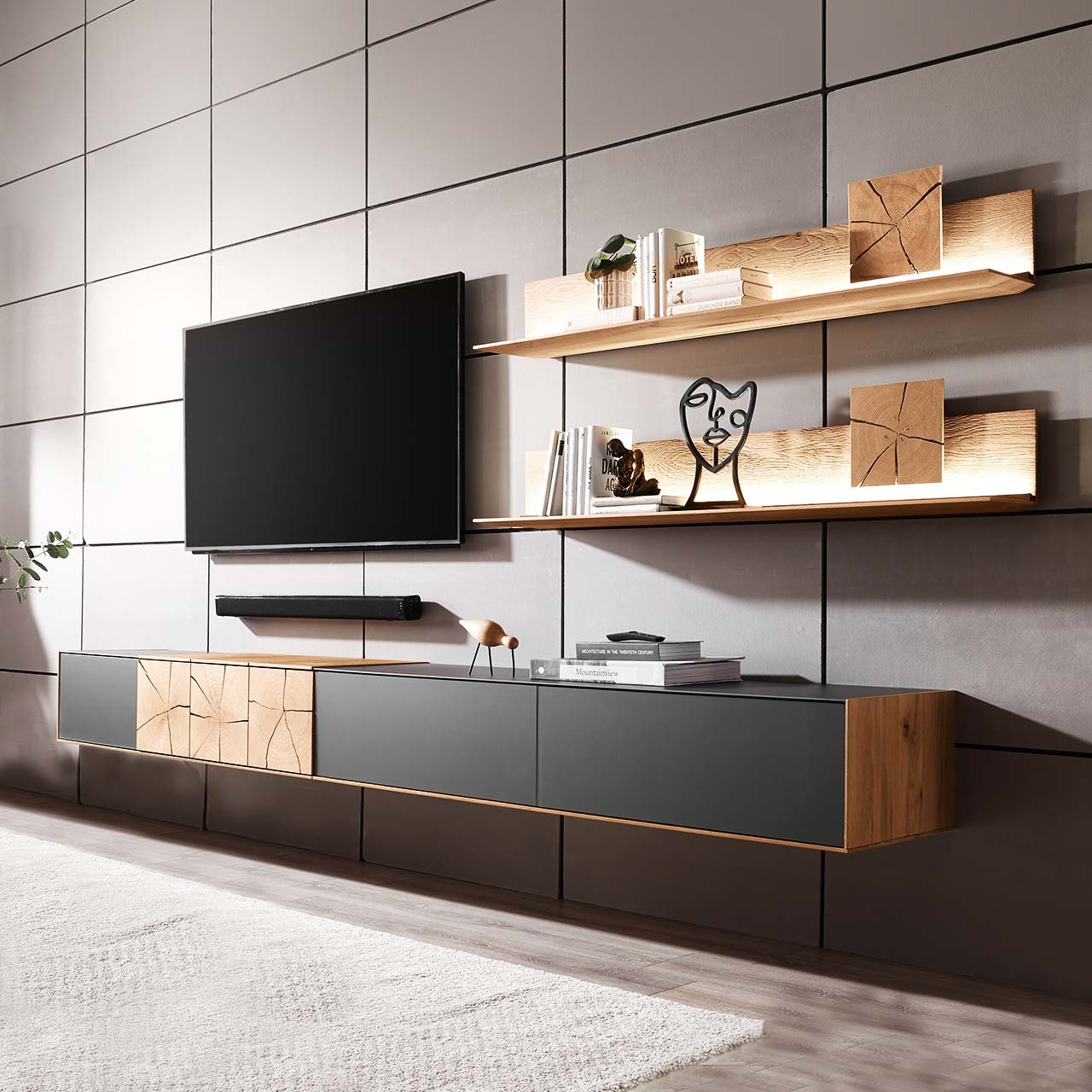 Moderne zweiteilige Massivholz Wohnkombination aus Kerneiche Umato mit Mattglas anthrazit Fronten, mit langem Hängelowboard und zwei Wandpaneelen mit dekorativen Hirnholzscheiben. Links daneben hängender Fernseher.