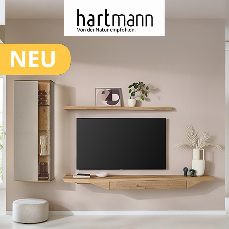 Hartmann SVEA - Massivholzmöbel aus Kerneiche Natur kombiniert mit Lack Sand und Riffholz. Ambientebild zeigt Hängelowboard, Wandboard und beleuchtete Hängevitrine im asymmetrischem Design.