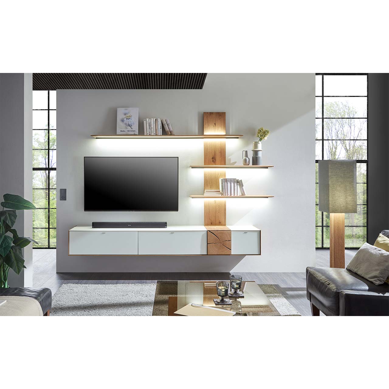 Wohnzimmer mit TV und moderner Wohnwand aus massiver Kerneiche Umato mit  Mattglas weiß Fronten und Hirnholzscheiben, mit langen Hängelowboard und Wandpaneel mit drei Regalböden. Im Vordergrund passender Couchtisch mit rechteckiger Glasplatte.