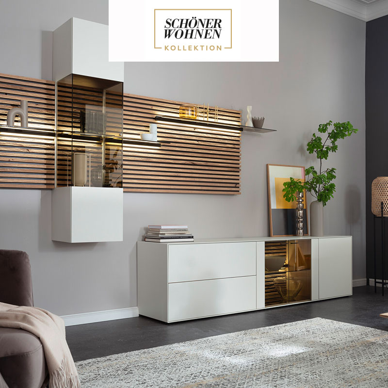 Hartmann YONNA - Wohn und Garderobenmöbel aus Birke weiß lackiert kombiniert mit Kerneiche Natur und Holzlamellen. Ambientebild zeigt ein weißes Hängelowboard und weiße, edle Hängevitrine eingefasst in ein Holz-Lamellenpaneel mit beleuchteten Glasböden.