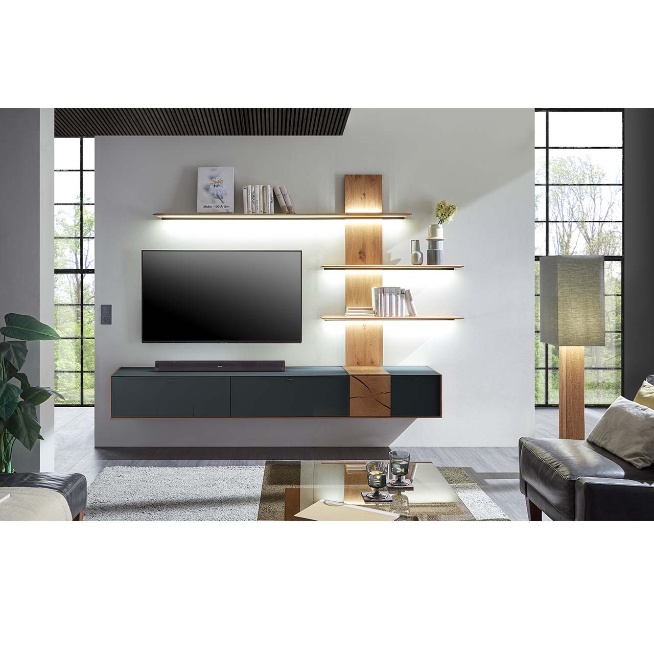 Wohnzimmer mit TV und moderner Wohnwand aus massiver Kerneiche Umato mit  Mattglas anthrazit Fronten und Hirnholzscheiben, mit langen Hängelowboard und Wandpaneel mit drei Regalböden. Im Vordergrund passender Couchtisch mit rechteckiger Glasplatte.