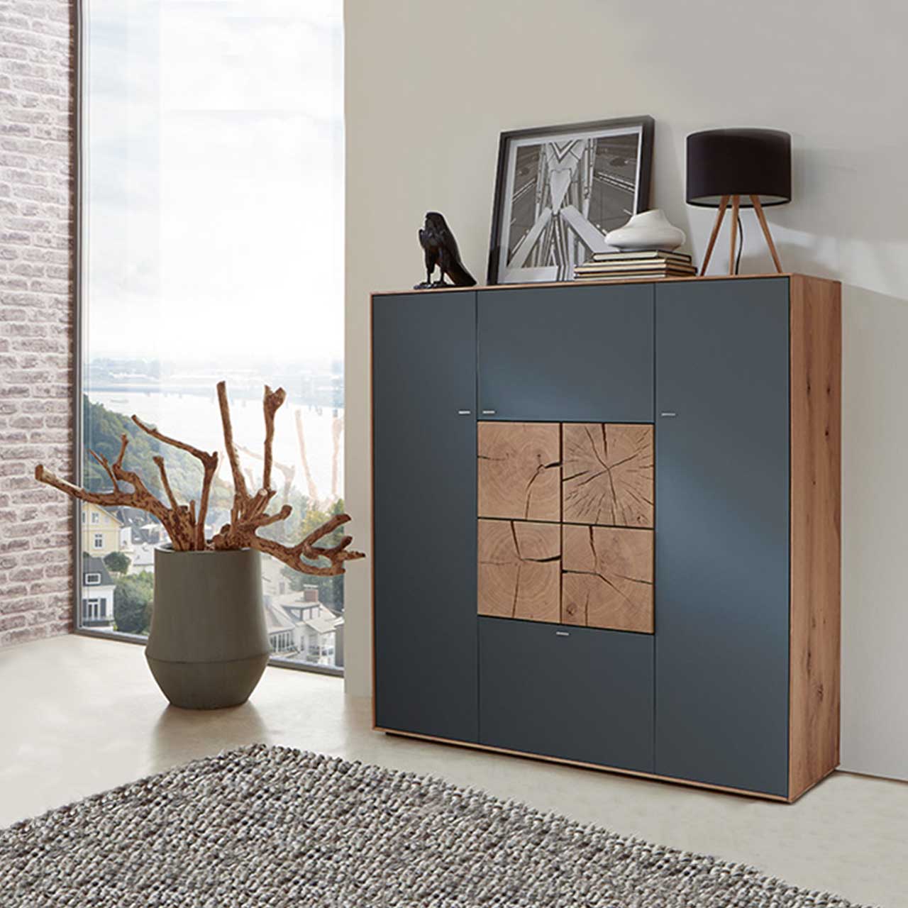 Modernes Highboard aus massiver Kerneiche Umato mit Mattglas anthrazit Fronten und vier in der Mitte zum Quadrat zusammengesetzten, dekorativen Hirnholzscheiben in heller Kerneiche Umato - in einem modernen Flur stehend.