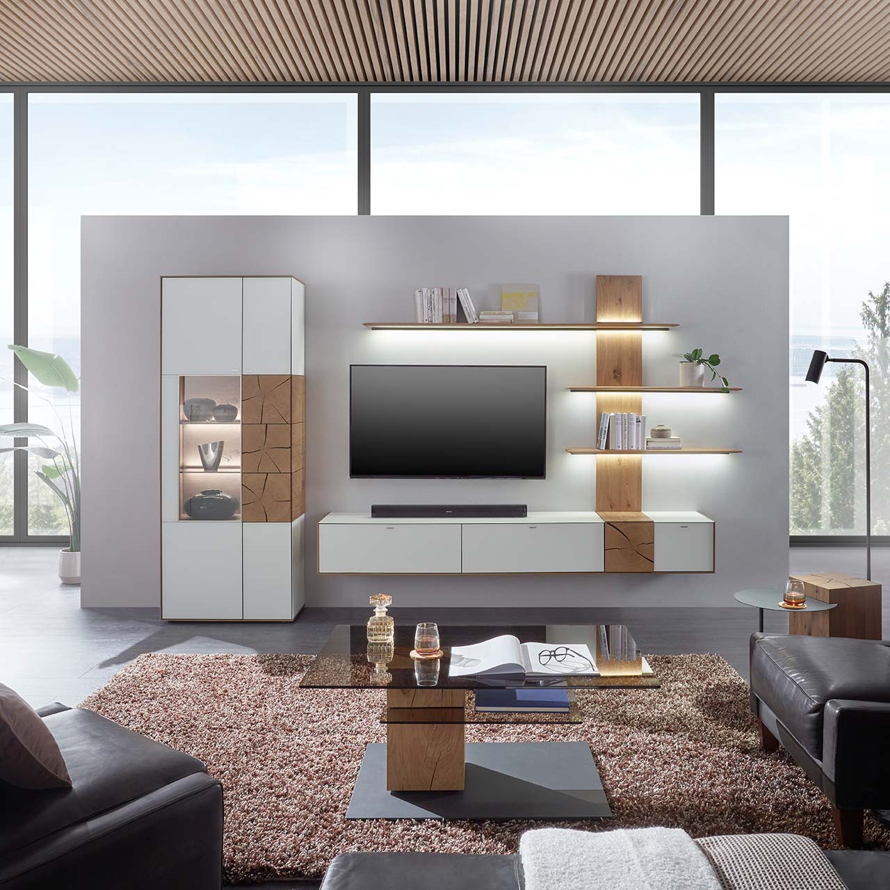 Moderne Wohnwand aus massiver Kerneiche mit Mattglas weißen Fronten, mit Hängelowboard, Wandpaneel mit Regalböden und Standvitrine. Im Vordergrund der passende Couchtisch mit rechteckiger Glasplatte.