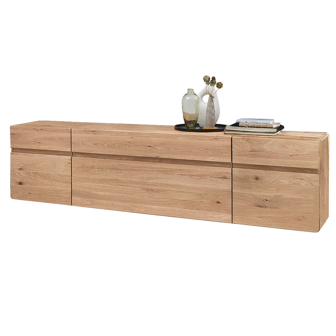 Hartmann VIDA - Lowboard 8630-3211 - Kerneiche Natur Modernes Lowboard aus massiver Kerneiche Natur mit edler Holzmaserung und markanter Holzeinkerbung in der Möbelfront. Lowboard hat zwei Holztüren rechts und links, mittig einen Schubkasten oben und eine Holzklappe unten.