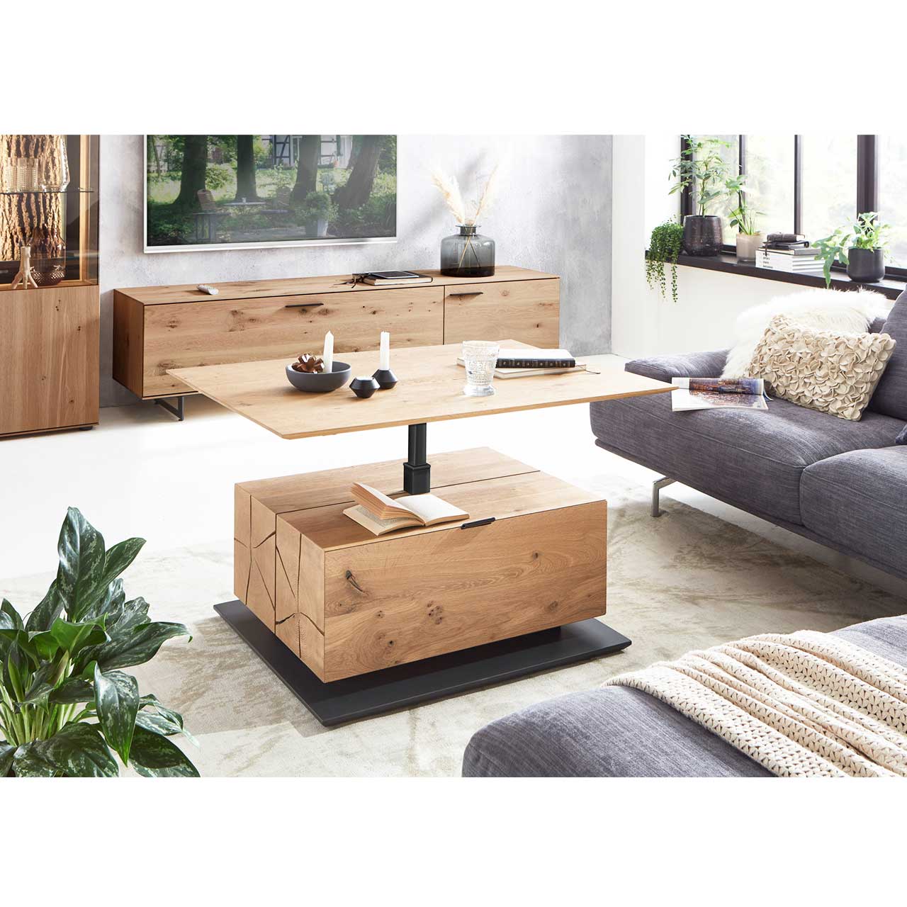 Moderner Couchtisch mit hochgefahrener Tischplatte, Hirnholzblock aus massiver Kerneiche, Klappe und Stauraumfach auf dunkler Bodenplatte – im Wohnzimmer stehend.