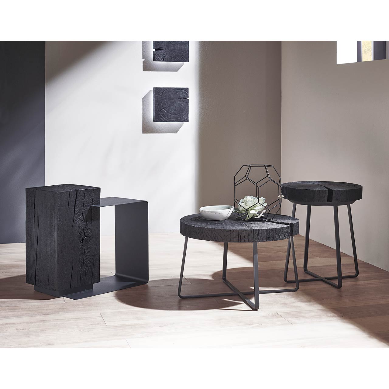 Modernes Wohnzimmer mit zwei runden Beistelltischen aus Kernesche anthrazit und filigranem Metallgestell, links daneben passender Beistelltisch mit dunklem Holzkorpus und Metallablage.