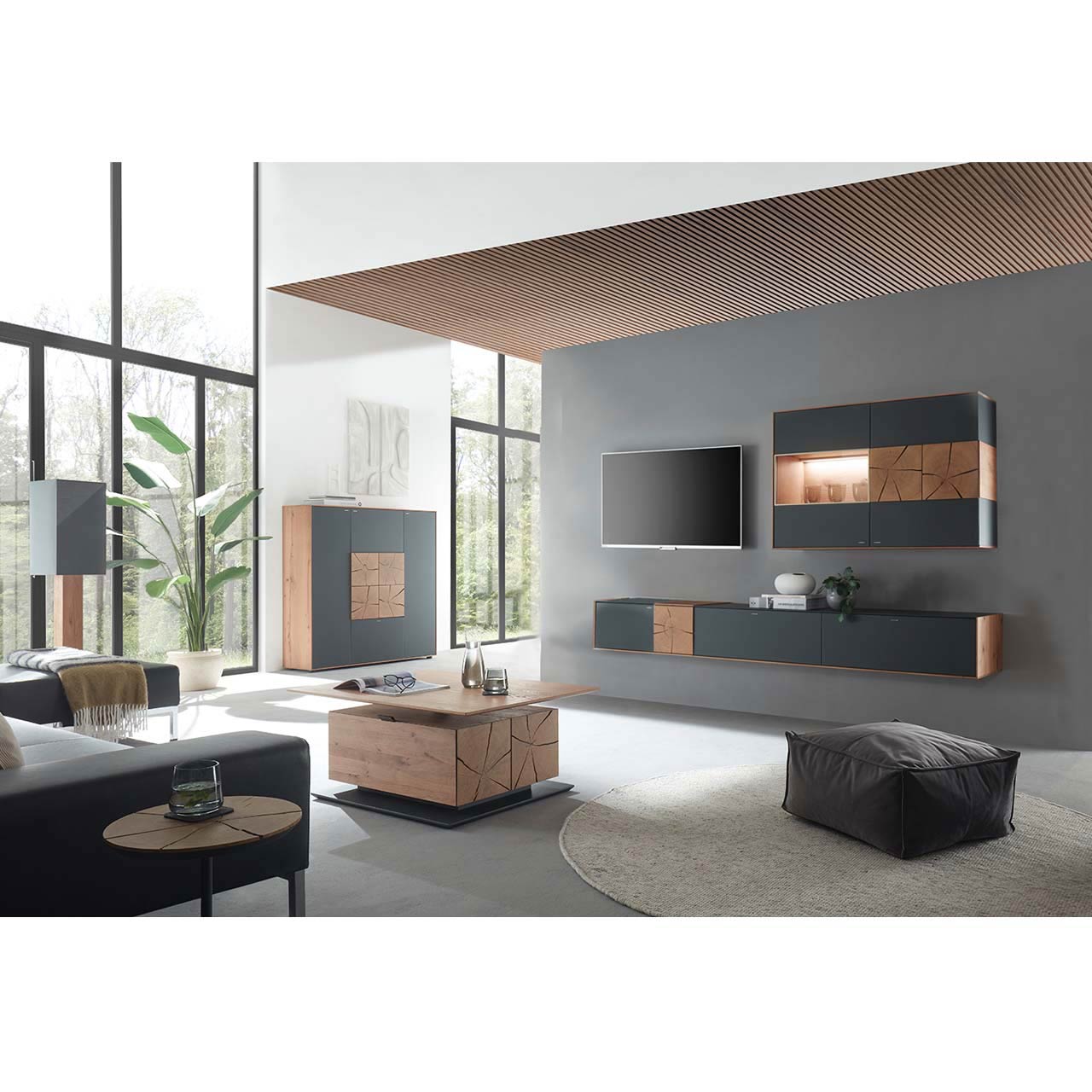 Wohnzimmer mit TV und moderner Wohnwand aus massiver Kerneiche und Mattglas anthrazit Fronten, mit schmalem Hängelowboard und beleuchteter Hängevitrine. Links das passende Highboard. Im Vordergrund ein rechteckiger Holz-Couchtisch.