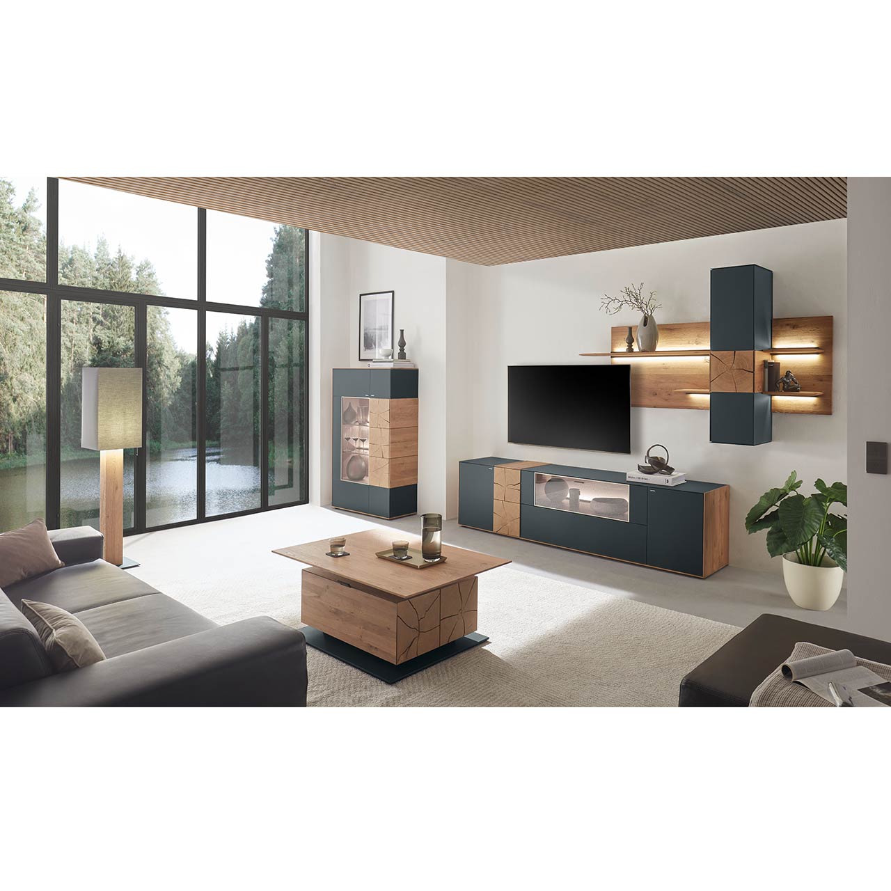 Moderne Wohnwand aus massiver Kerneiche mit anthrazitfarbenen Fronten, mit Lowboard mit Glasausschnitt sowie Wandpaneel mit Regalböden und Hängeschrank. Links ein Highboard mit Glasfront und Hirnholzscheiben. Im Vordergrund der passende Couchtisch. 