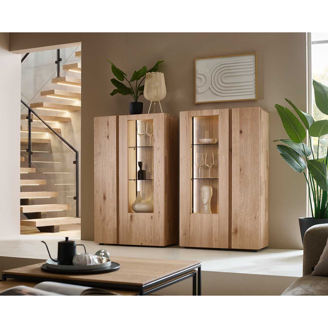 Zwei moderne Highboards aus massivem Eichenholz mit je zwei geschlossen Holz - und Glas/Holztüren. Hinter der Glasfront sichtbar die edel geschoppte Rückwand und je zwei beleuchteten Glaseinlegeböden - im Wohnzimmer stehend.