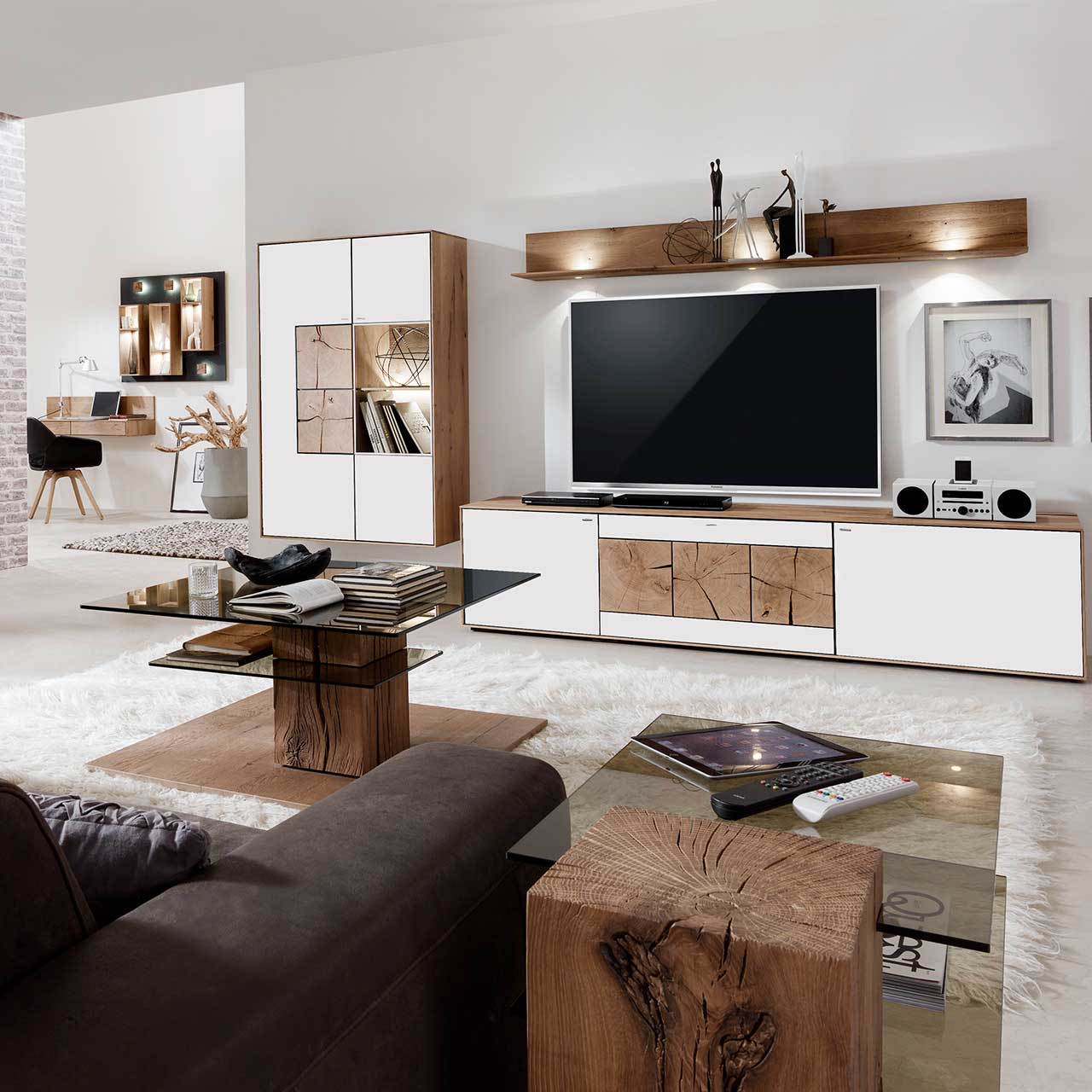 Wohnzimmer mit TV und moderner Wohnwand aus massiver Kerneiche Umato mit Mattglas weiß Fronten: Langes Lowboard mit dekorativen Hirnholzscheiben, Hängeregal aus Kerneiche, Hängevitrine mit beleuchtetem Glasausschnitt und Hirnholz.