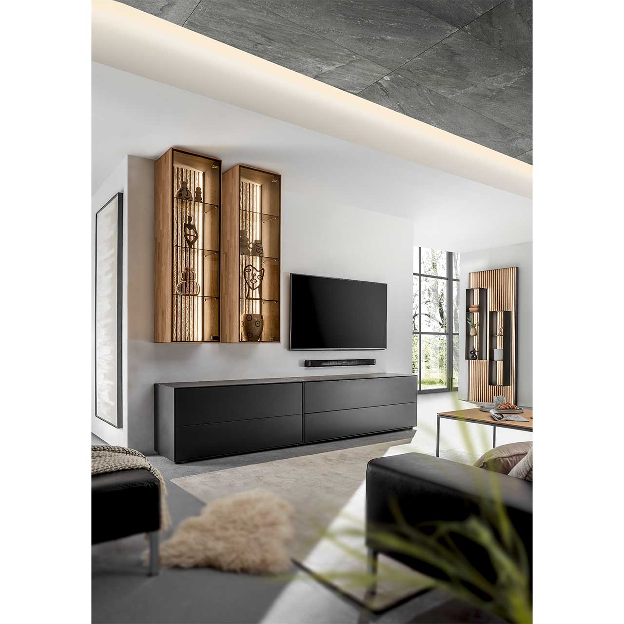 Stilvolles Wohnzimmer mit vierteiliger Wohnwand in Birke Anthrazit und heller Kerneiche mit Lamellen. Mit passendem Wandpaneel rechts und minimalistischem Couchtisch im Vordergrund.