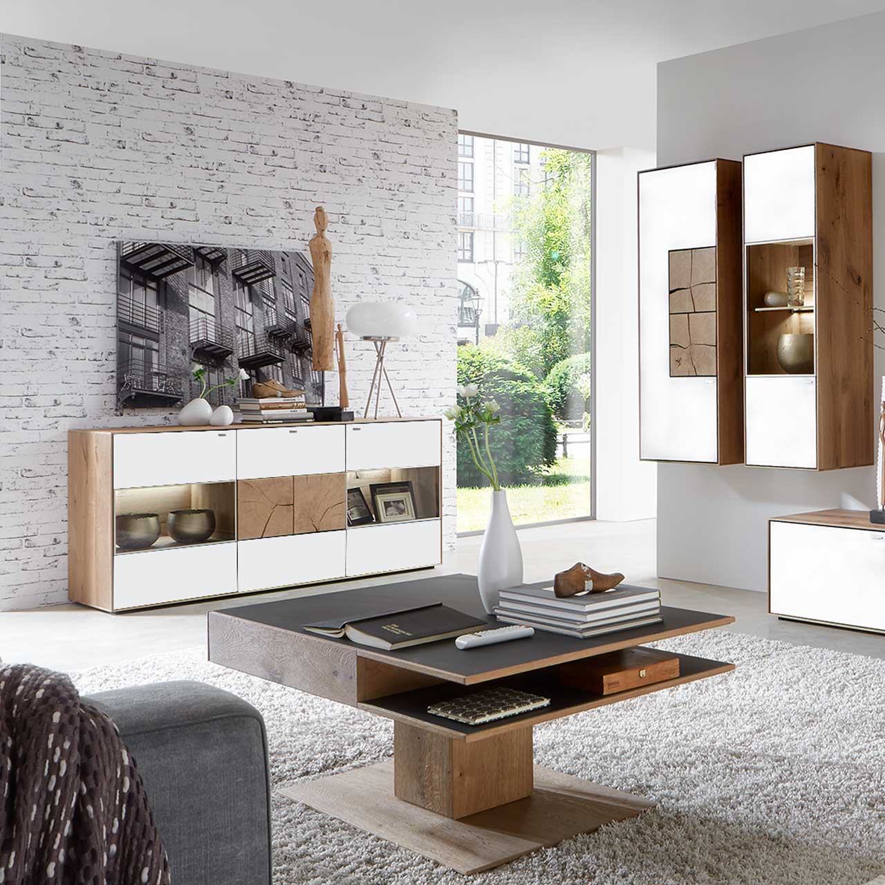 Wohnzimmer mit modernen Massivholzmöbel aus Kerneiche Umato mit Mattglas weiß Fronten: Hängeschrank mit Hirnholzscheiben, beleuchtete Hängevitrine, links modernes Sideboard mit Glasfront und Hirnholzscheiben, davor passender Couchtisch.