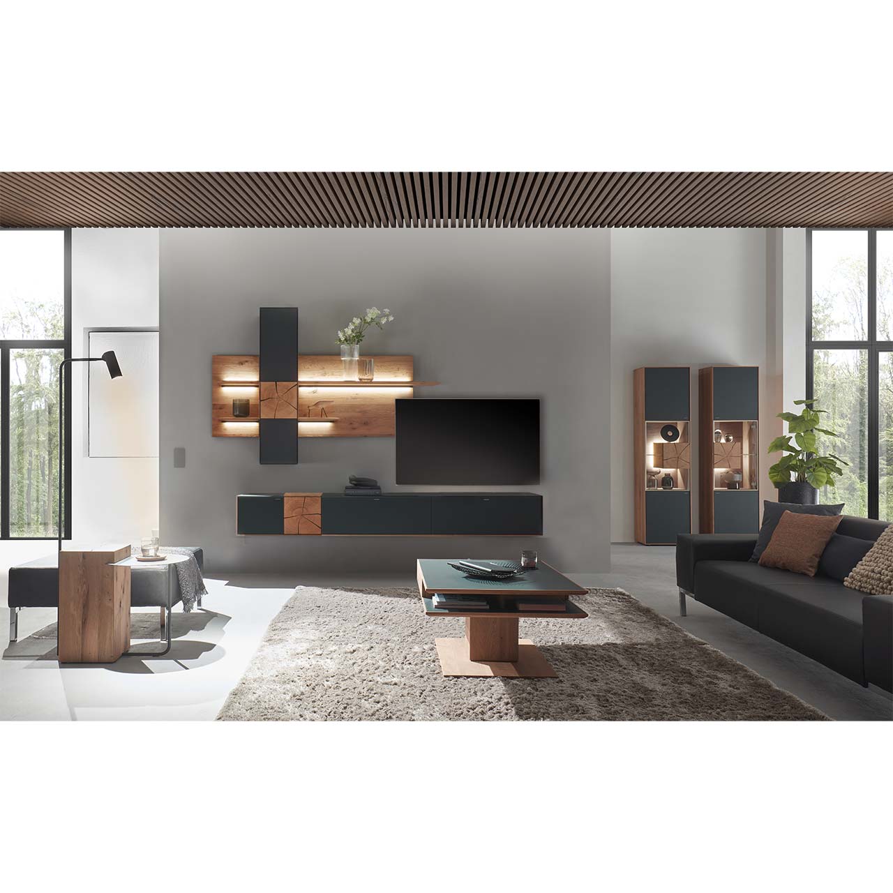 Wohnzimmer mit TV und moderner Wohnwand aus massiver Kerneiche mit Hirnholz und Mattglas anthrazit Fronten, mit Hängelowboard, Wandpaneel mit Regalböden und Hängeschrank. Hinten rechts zwei passende Standvitrinen. Im Vordergrund rechteckiger Couchtisch.