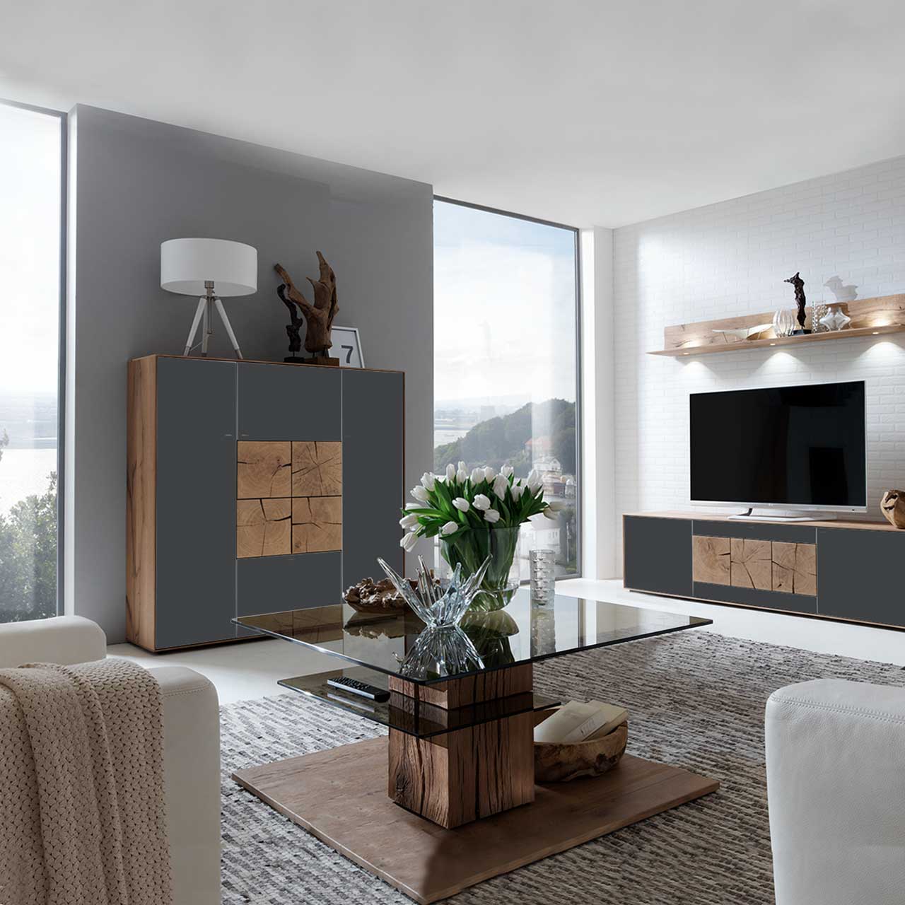 Milieubild Hartmann CAYA - Highboard 7170-7133A Modernes Highboard aus massiver Kerneiche Umato mit Mattglas anthrazit Fronten und vier dekorativen, rechteckigen Hirnholzscheiben in heller Kerneiche Umato mittig platziert - in einem Wohnzimmer stehend, davor passender Glas-Couchtisch.