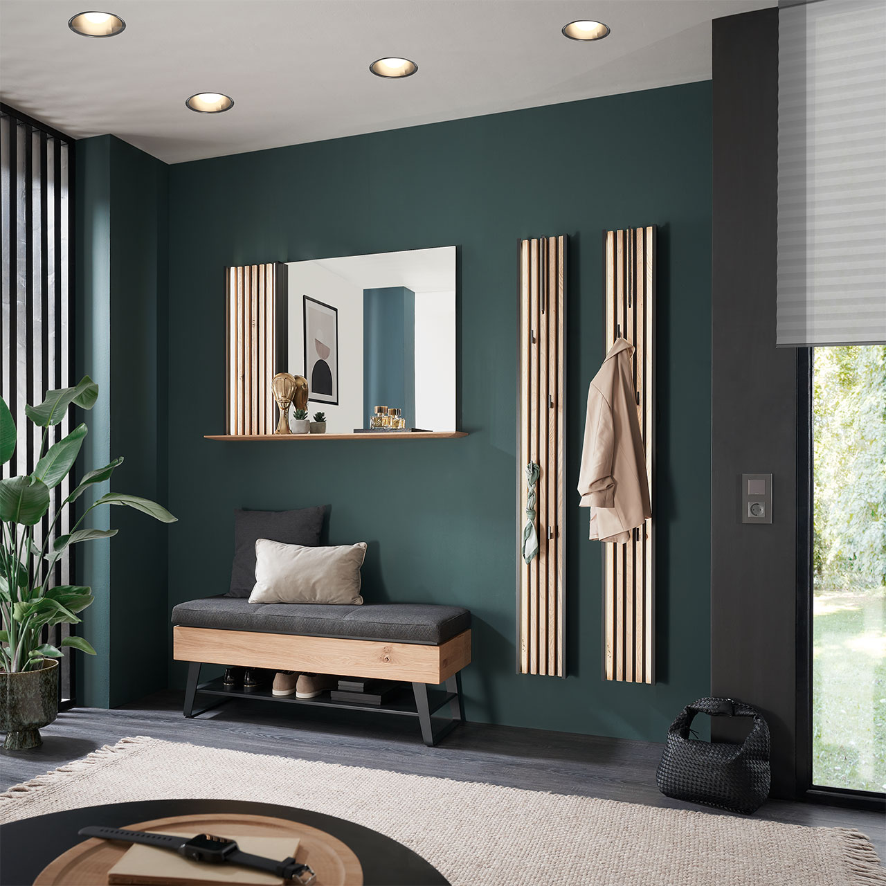Flur mit modernen Garderobenmöbeln aus massiver Kerneiche Natur: Ein Spiegelpaneel mit Lamellen-Akzent, zwei Garderobenpaneele mit Lamellen-Rückwand und Kleiderhaken und eine gepolsterte Sitzbank auf Metallkufen mit Stauraumfach.
