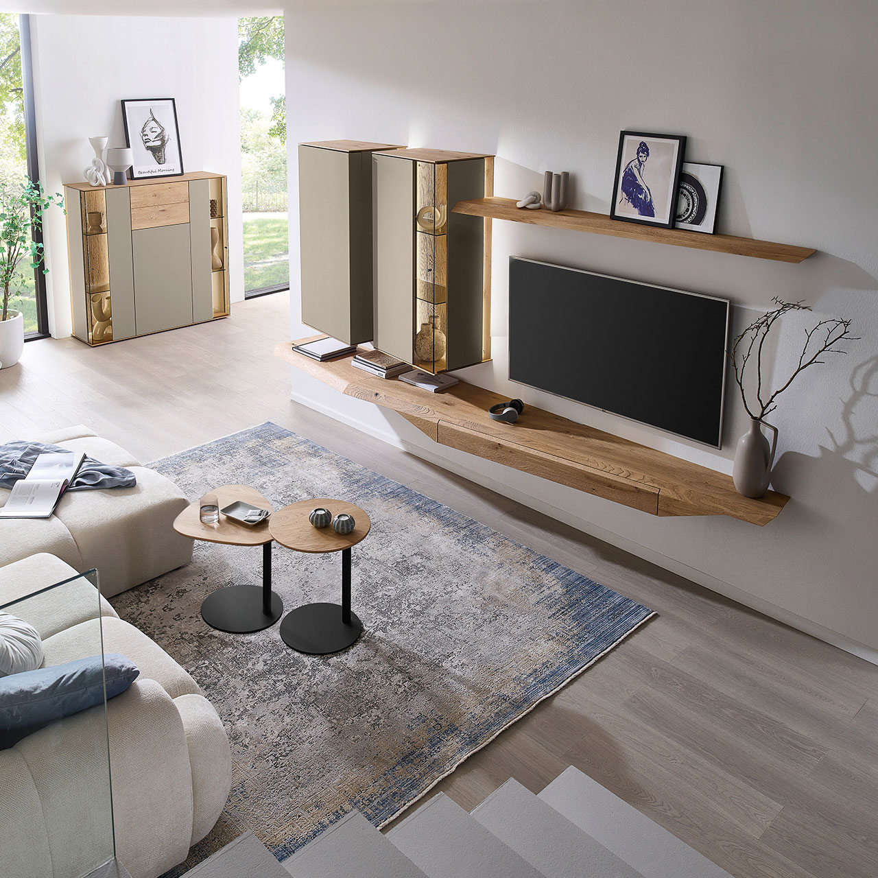 Hartmann Möbel SVEA - Wohnwand 8660 Nr. V26 - vierteilig aus Kerneiche Natur, Lack Sand - Milieubild Wohnzimmer mit moderner Massivholzwohnwand bestehend aus Hängelowboard, Hängevitrine, Hängeschrank sowie Wandboard - im asymmetrischen Design. Links passendes Highboard mit Glastüren, davor zwei Beistelltische aus Holz - Ansicht von oben.