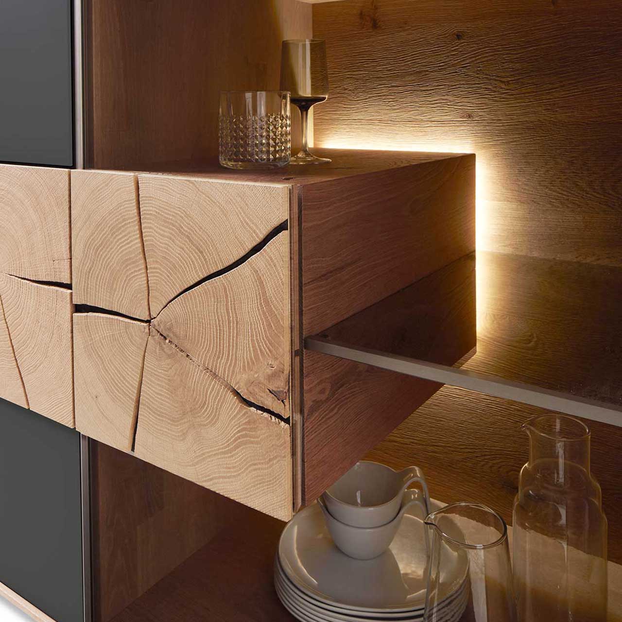 Detailbild eines beleuchteten Hirnholzblocks aus massiver Kerneiche Umato mit sichtbarer Holzmaserung und charakteristischen Holzrissen an Glastür eines CAYA Sideboards oder einer Hängevitrine. 