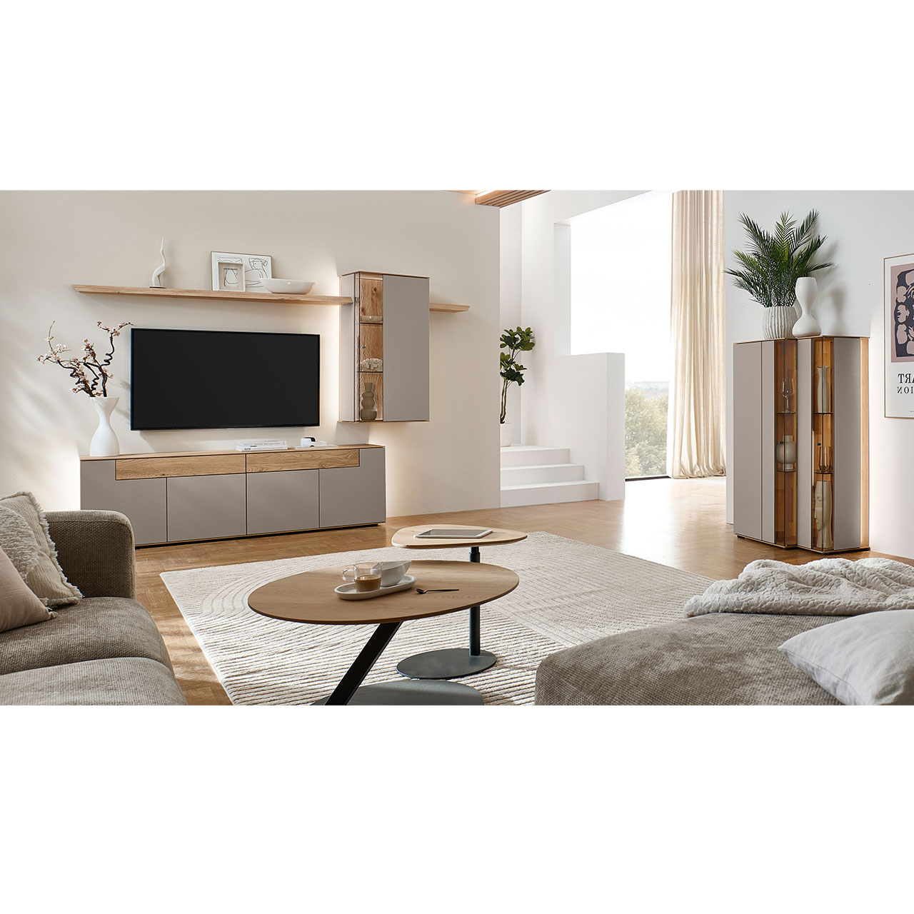 Hartmann Möbel SVEA - Wohnkombination 8660 Nr. V34 SV - vierteilig aus Kerneiche Natur, Lack Sand - Milieubild Wohnzimmer mit moderner Massivholzwohnwand bestehend aus einem Lowboard mit Schubkästen, einer Hängevitrine sowie zwei Wandboarden mit Holzboden - im asymmetrischen Design. Rechts passendes Highboard, davor Holz-Couchtisch.
