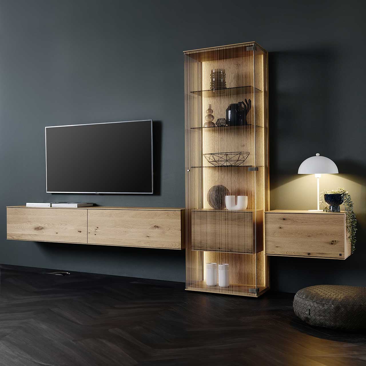 LINEA Leonardo Living - Wohnwand 8540 Nr. V20 Modernes Wohnzimmer mit Fernseher und dreiteiliger Wohnwand aus Kerneiche Natur: Zwei schlichte Hängelowboard und Standvitrine mit satiniertem Glas und innenliegendem Holzkorpus mit Klappe – platziert vor einer dunklen Wand.