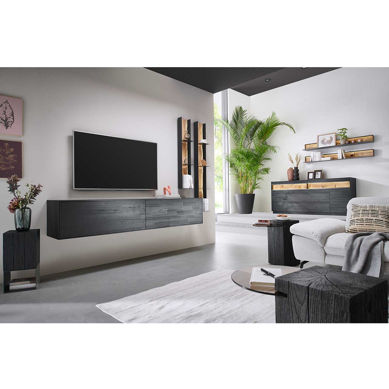 Modernes Wohnzimmer mit dreiteiliger Wohnwand aus massiver Kernesche anthrazit: Hängelowboard und zwei Wandregale. Links das passende Sideboard mit Wandpaneelen. Im Vordergrund zwei dazugehörige Beistelltische. 