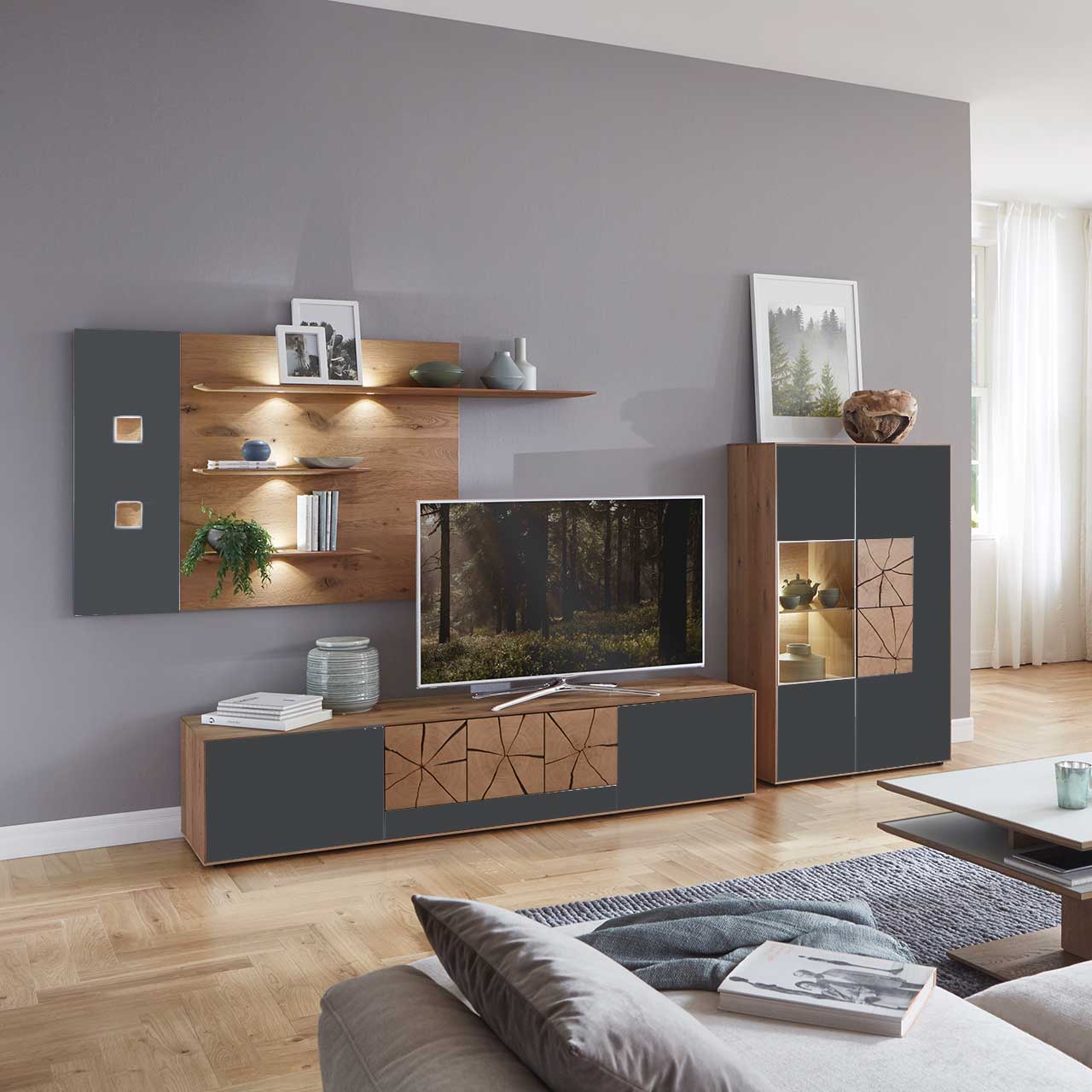 Wohnzimmer mit moderner dreiteiliger Massivholz Wohnwand mit Mattglas Anthrazit Fronten und dekorativen Hirnholzscheiben: Langes Lowboard mit Hirnholz und Kufen, Wandpaneel mit Regalböden, Highboard mit beleuchtetem Glasausschnitt und Hirnholz.